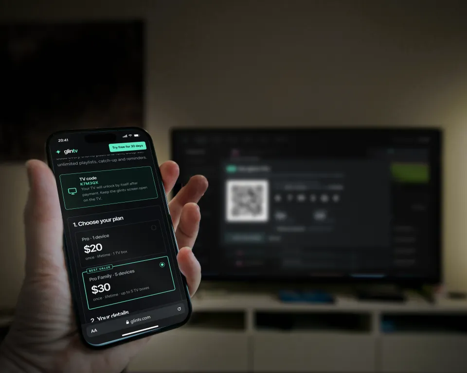 A hand holding a phone with the glintv Pro checkout page; behind it the TV shows the glintv QR code and the code K7M3QX