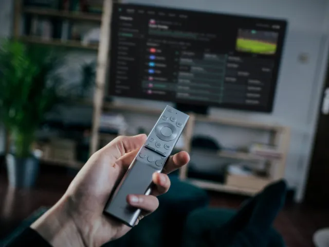 A hand holding a TV remote in a living room, with glintv on the TV